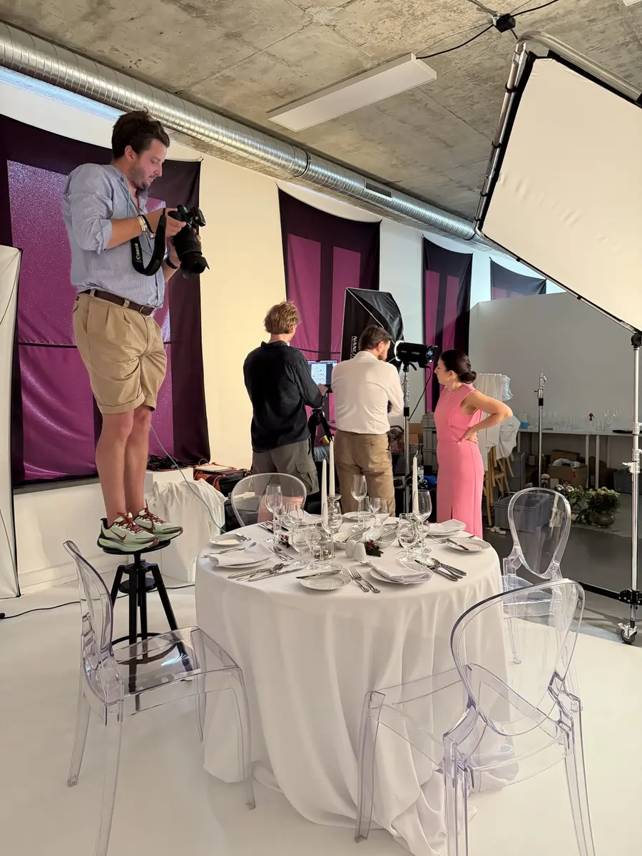 Fotograf na stołku fotografuje okrągły stół nakryty białym obrusem